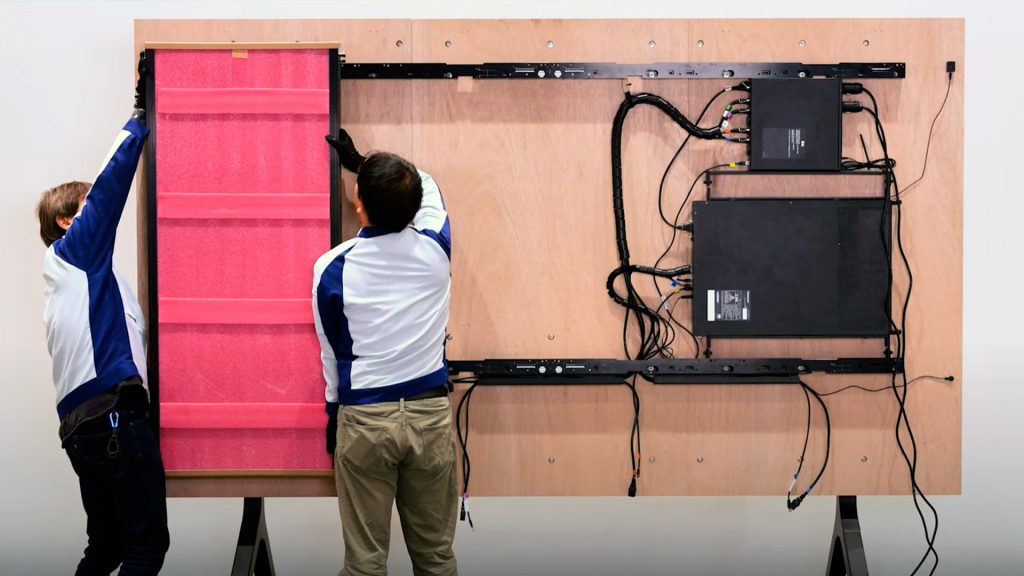 Two technicians install first panel of a LED display on wall