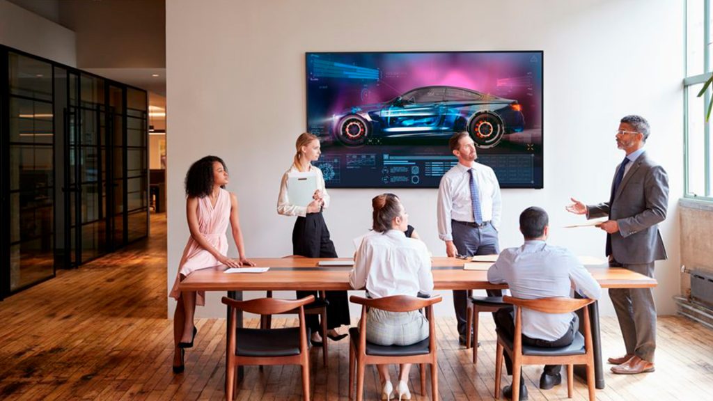 6 personer i mødesituation om bord med stor skærm på væggen bag dem