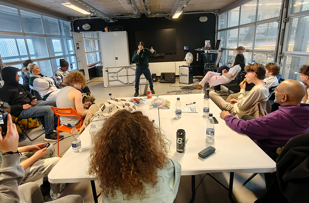 Mand synger i mikrofon foran unge mennesker, der sidder og kigger på ham